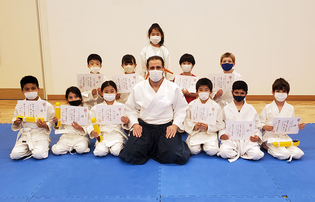 The proud teacher with his happy group of students holding their 11th kyu certificates and fitting yellow belt.